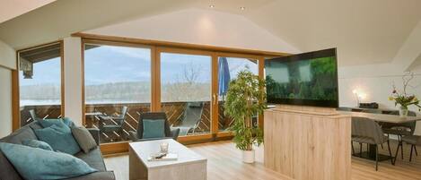 Una sala de estar moderna con un televisor grande, suelo de madera y vistas amplias a través de grandes ventanales.