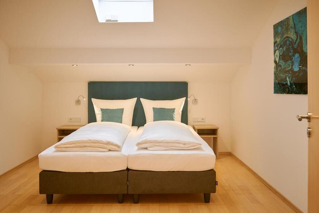 A bedroom with a bed, bedside tables, a painting, and a skylight.