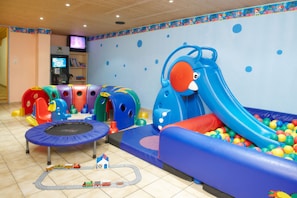 Un espace de jeux pour enfants avec un trampoline, des toboggans et une piscine à balles.