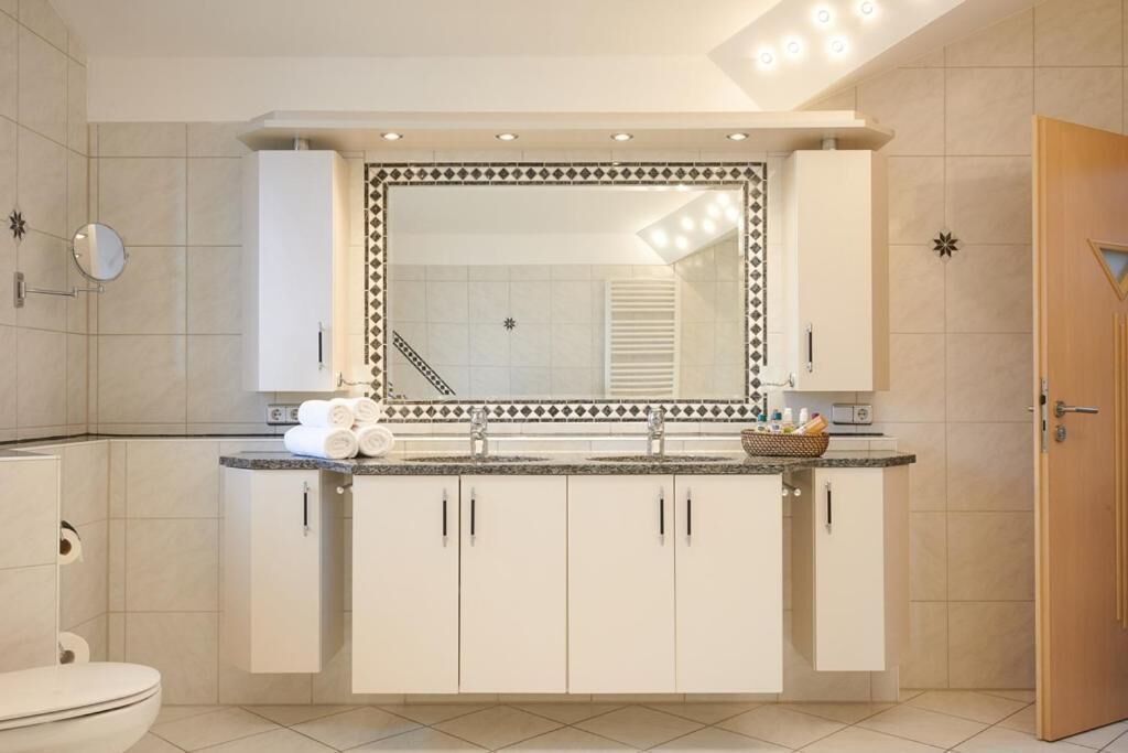 Une salle de bain avec un lavabo blanc, un miroir et des meubles de rangement, des toilettes et un espace douche.