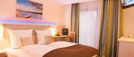 A hotel room with a large bed, a desk, a chair, a TV, and a window with curtains.