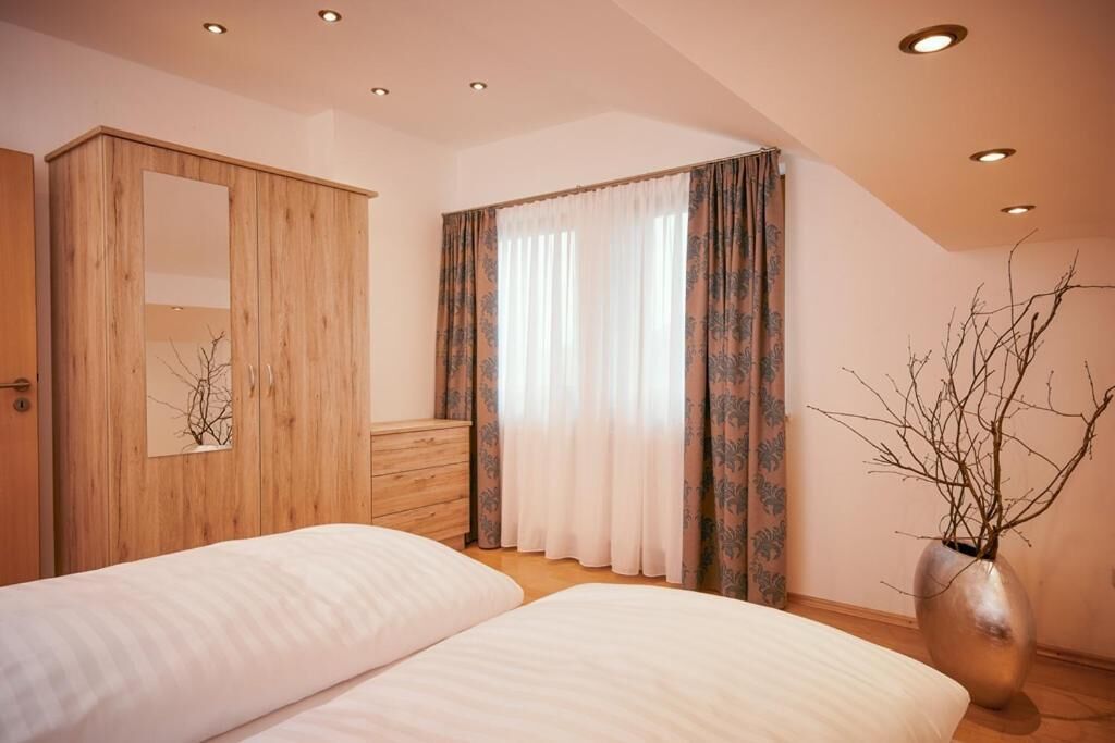 A bedroom with two beds, a wooden wardrobe, a mirror, and a window with curtains.
