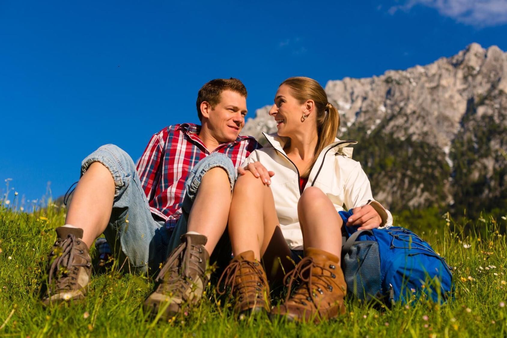 Twee personen zitten op het gras met een bergachtig landschap op de achtergrond.