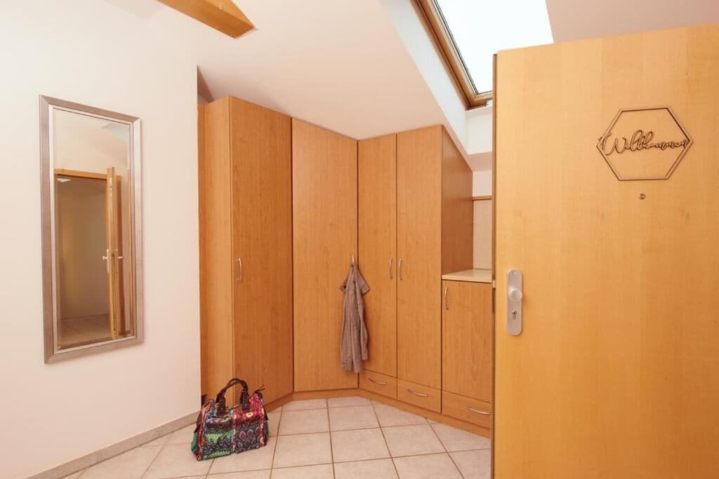 A room with wooden wardrobes, a door with a welcome sign, a mirror, and a tiled floor.