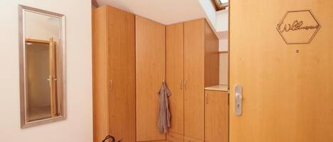 A room with wooden wardrobes, a door with a welcome sign, a mirror, and a tiled floor.