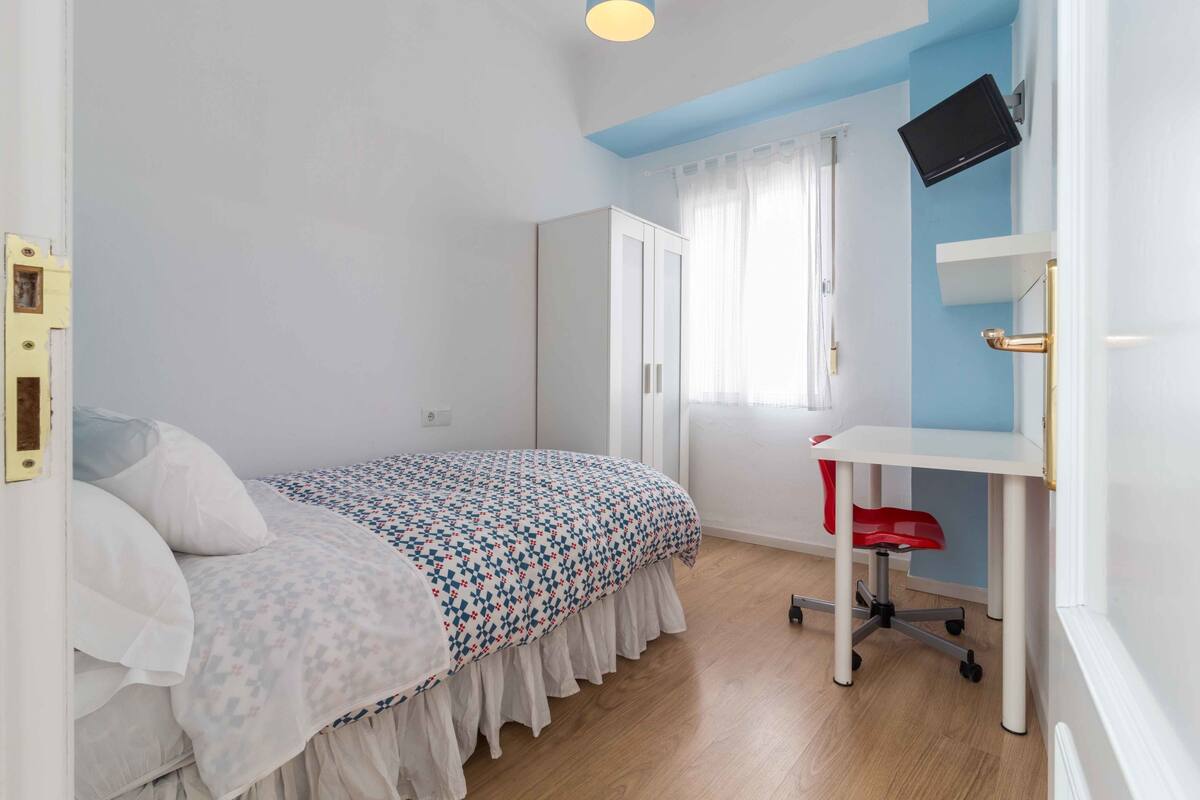 A bedroom with a bed, a desk, a chair, a TV, and a wardrobe.
