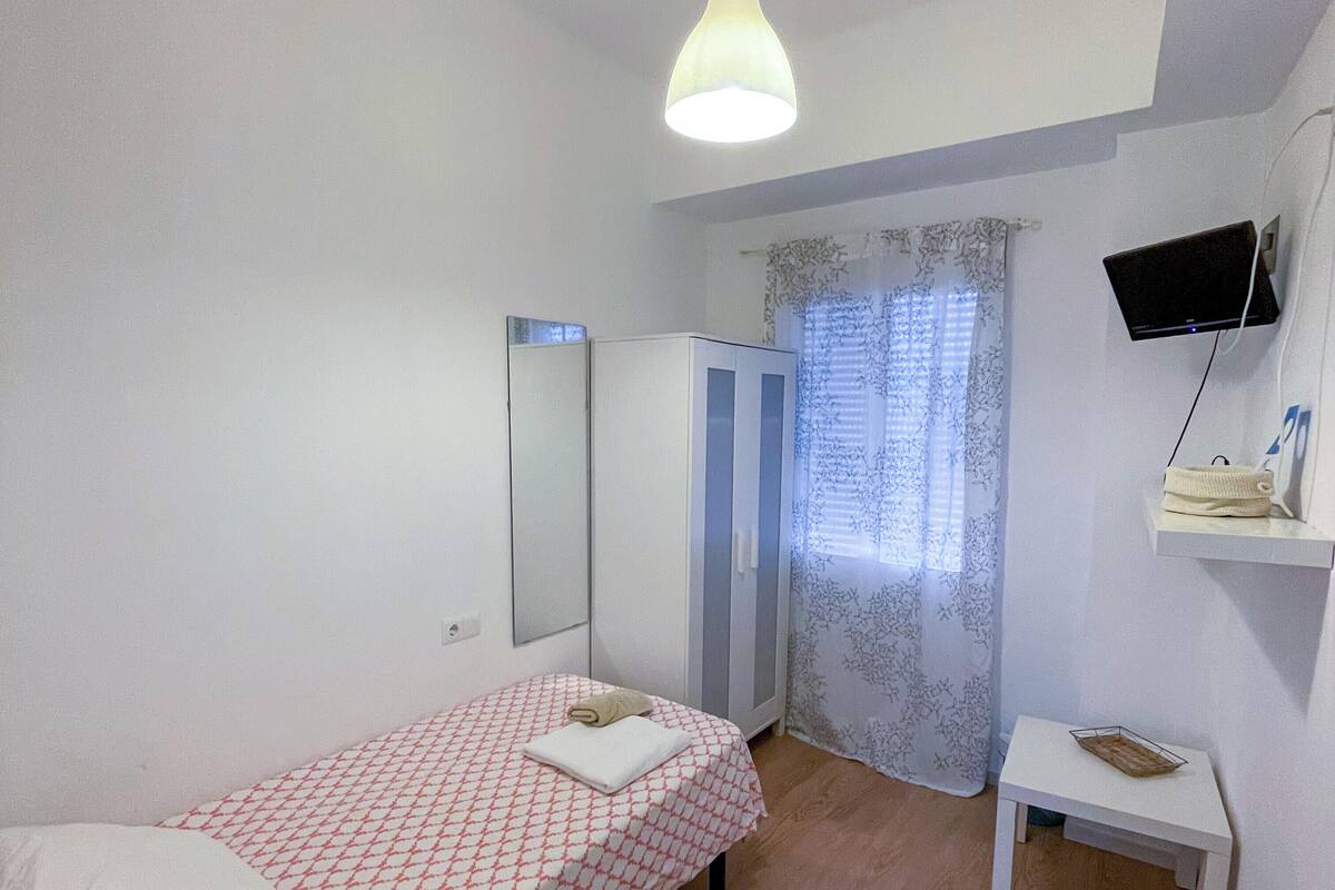 A bedroom with a bed, a wardrobe, a television mounted on the wall, and a small table.