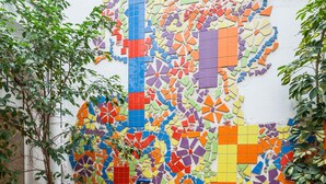 Una parete decorata con un mosaico colorato e motivi geometrici, con piante in vaso e un pavimento piastrellato.