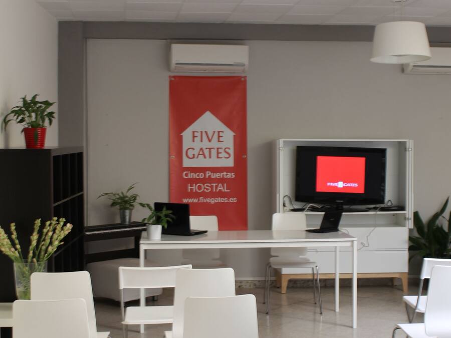 Un espace d’accueil avec une banderole rouge, des chaises blanches, un bureau, un téléviseur et un luminaire suspendu noir.