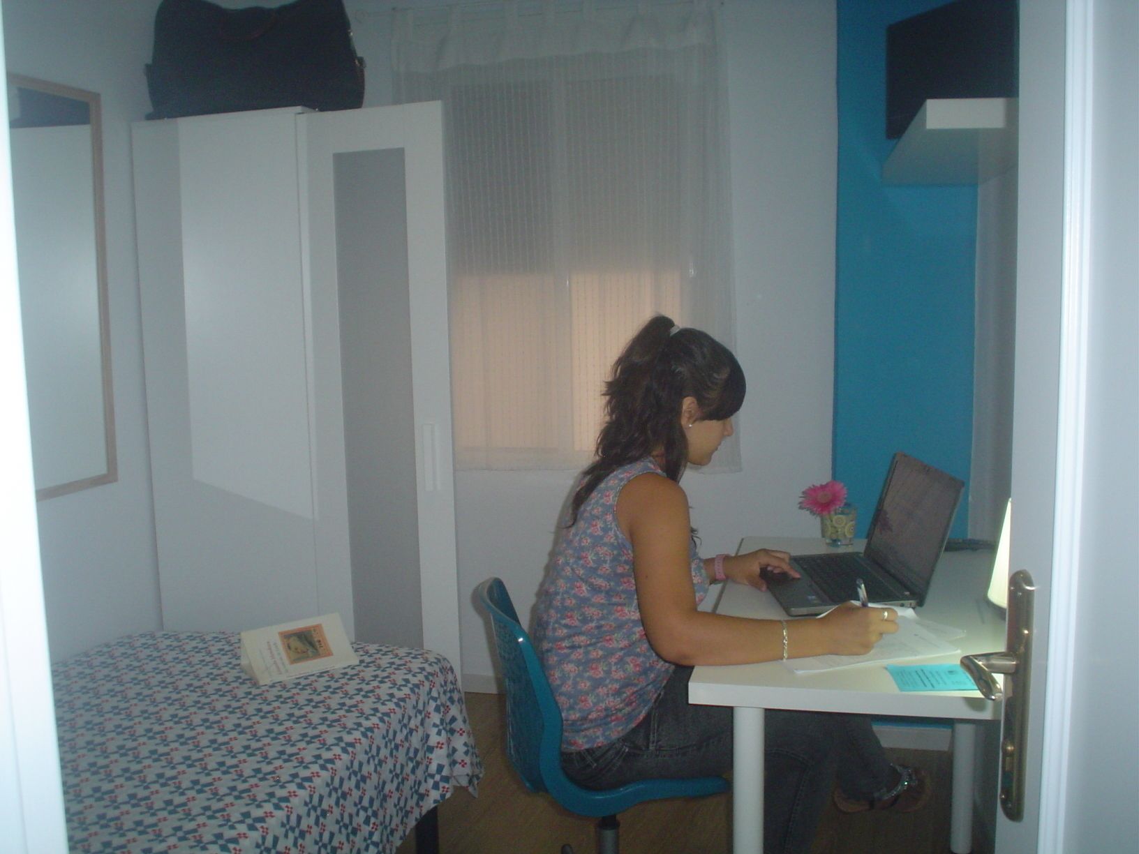 A room with a bed, a desk with a laptop, and a chair.