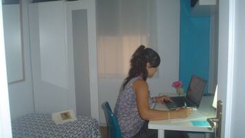 A room with a bed, a desk with a laptop, and a chair.
