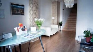 Una camera moderna con un tavolo rotondo in vetro, un divano bianco, carta da parati decorata, un lampadario e una scala che conduce a un altro piano.