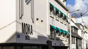 Een hotel genaamd MOKA HOTEL met een moderne gevel, grote ramen en een groene luifel.