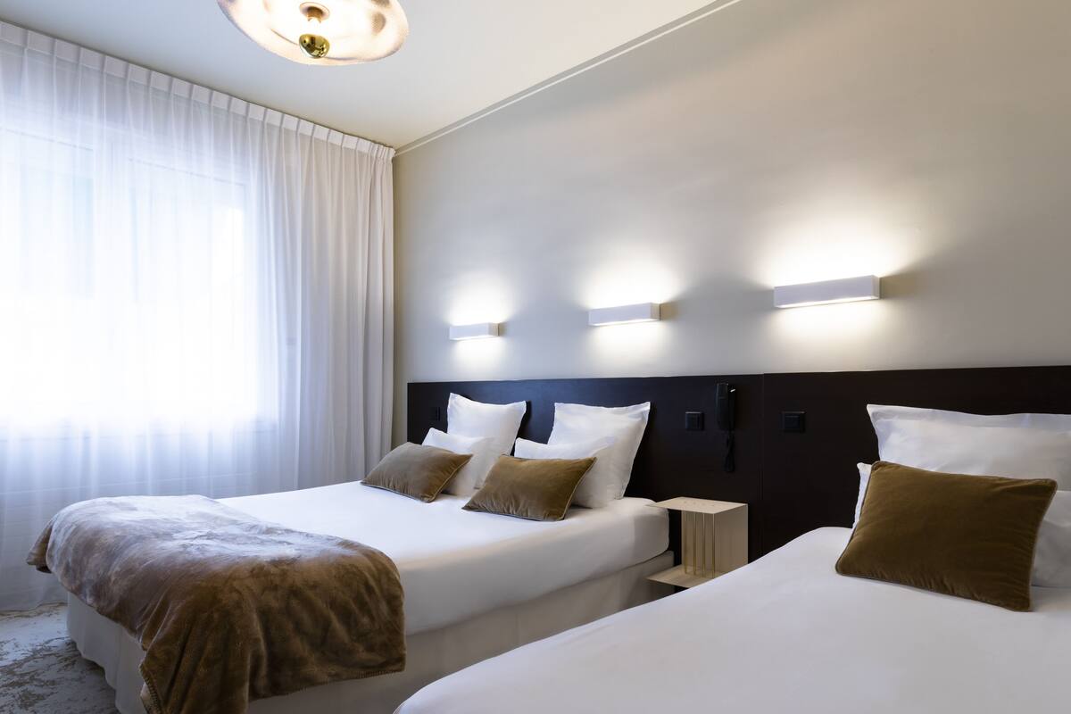 Habitación de hotel con dos camas, una mesita de noche, un teléfono y una ventana con cortinas.