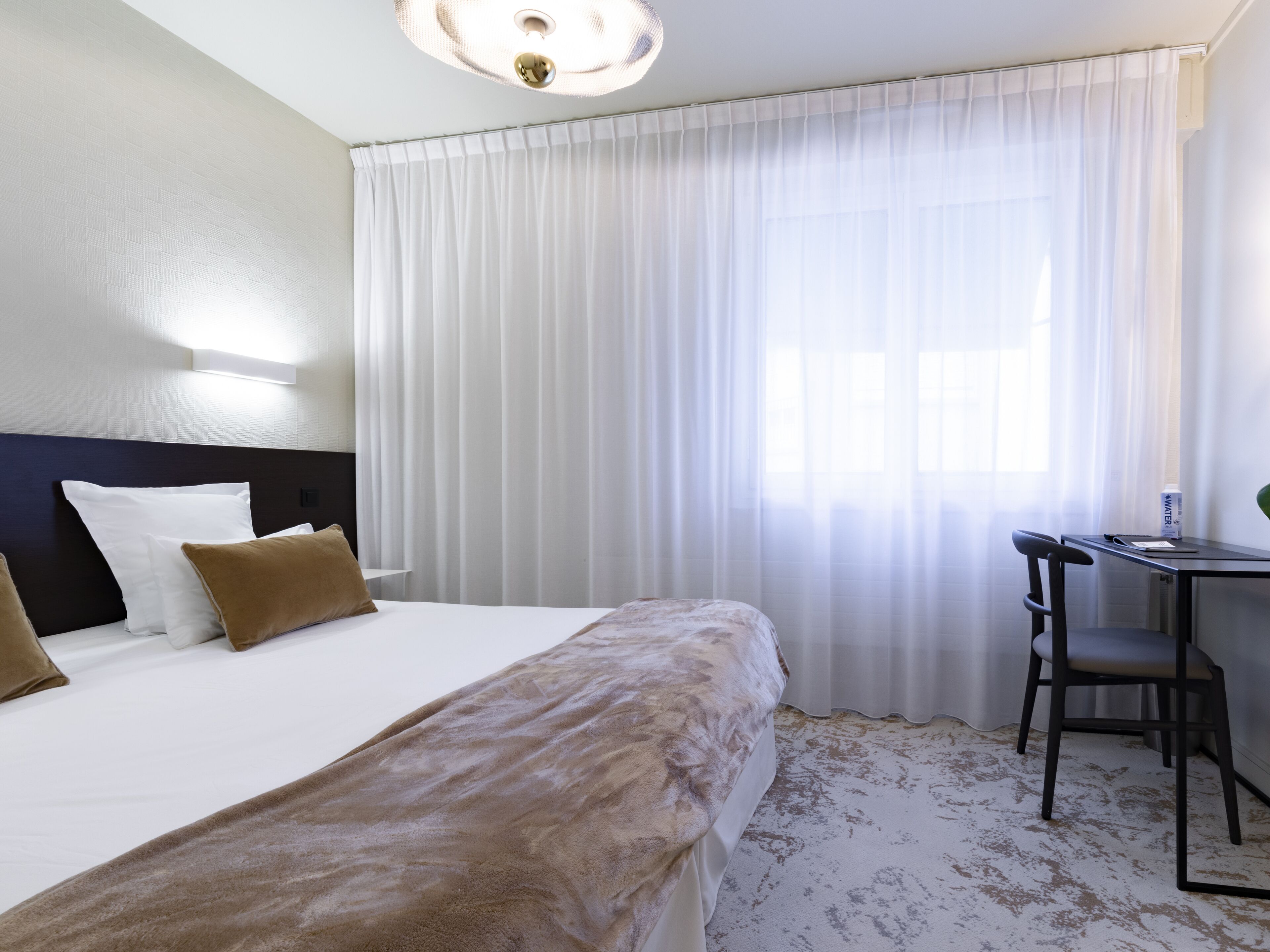 Una camera d'albergo con un letto, una scrivania, una sedia e una finestra con tende.