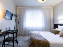 A hotel room with a bed, a desk, a chair, a television, and a large window with curtains.