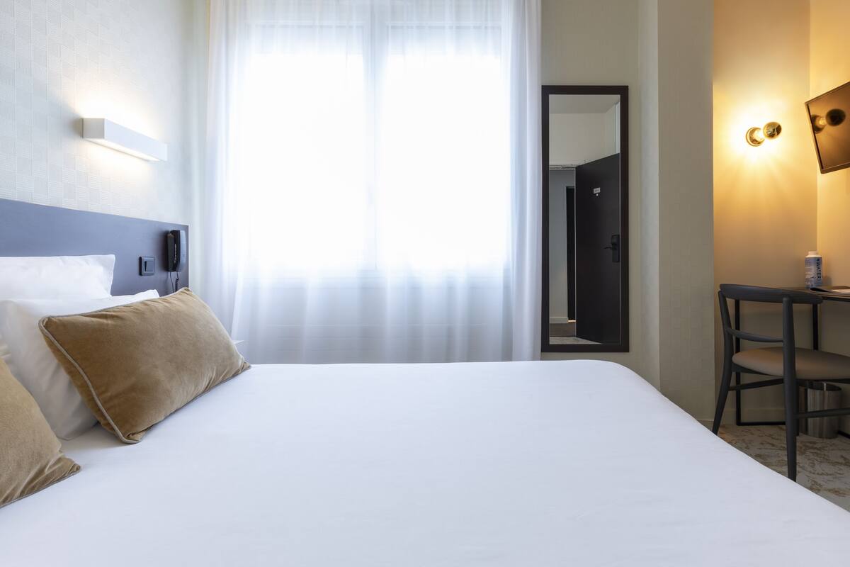 Una habitación de hotel con una cama grande, un escritorio, una silla, un teléfono y un espejo.