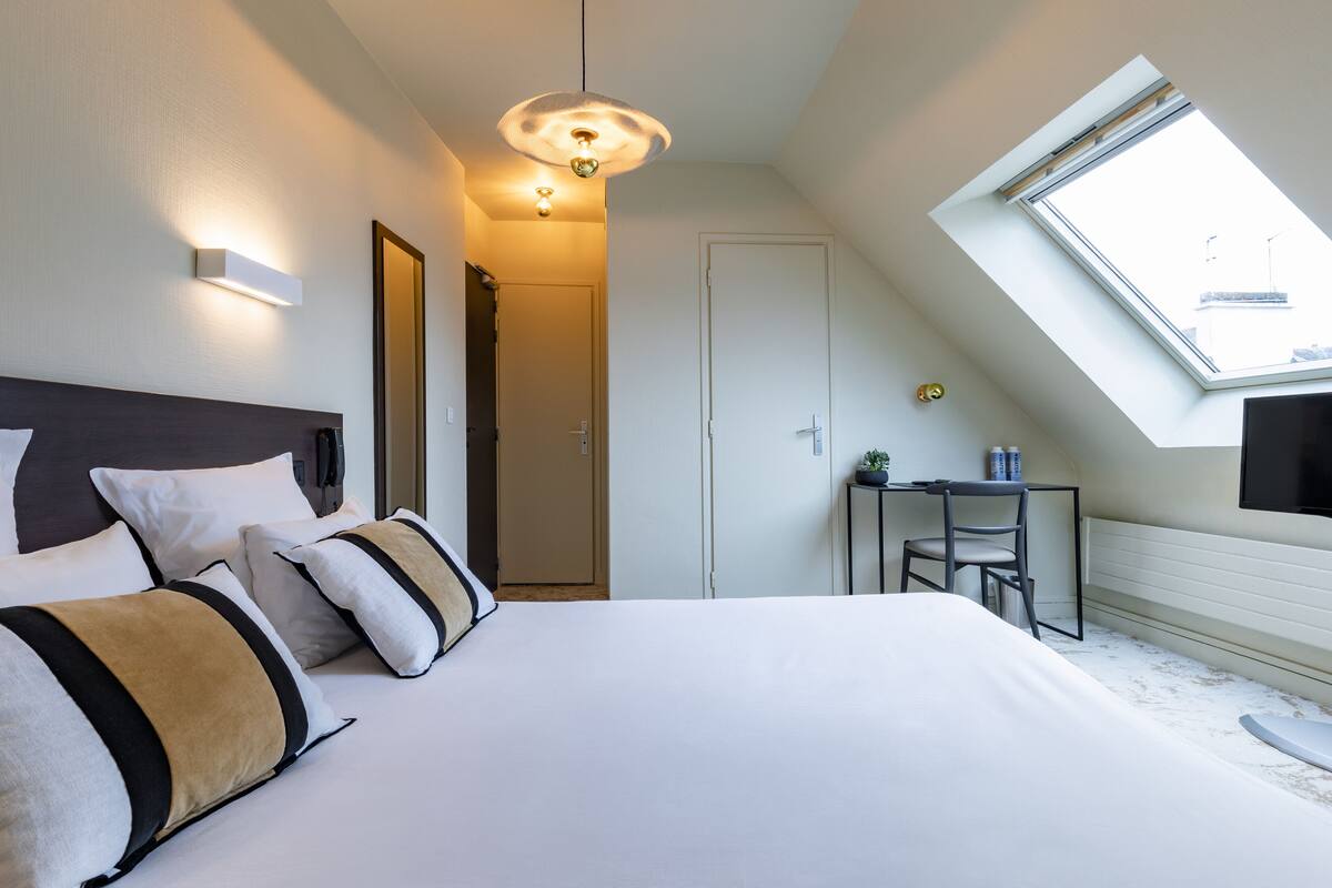 Habitación de hotel moderna con una cama grande, un escritorio, una silla, una mesita, un televisor y un tragaluz.