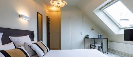 Habitación de hotel moderna con una cama grande, un escritorio, una silla, una mesita, un televisor y un tragaluz.