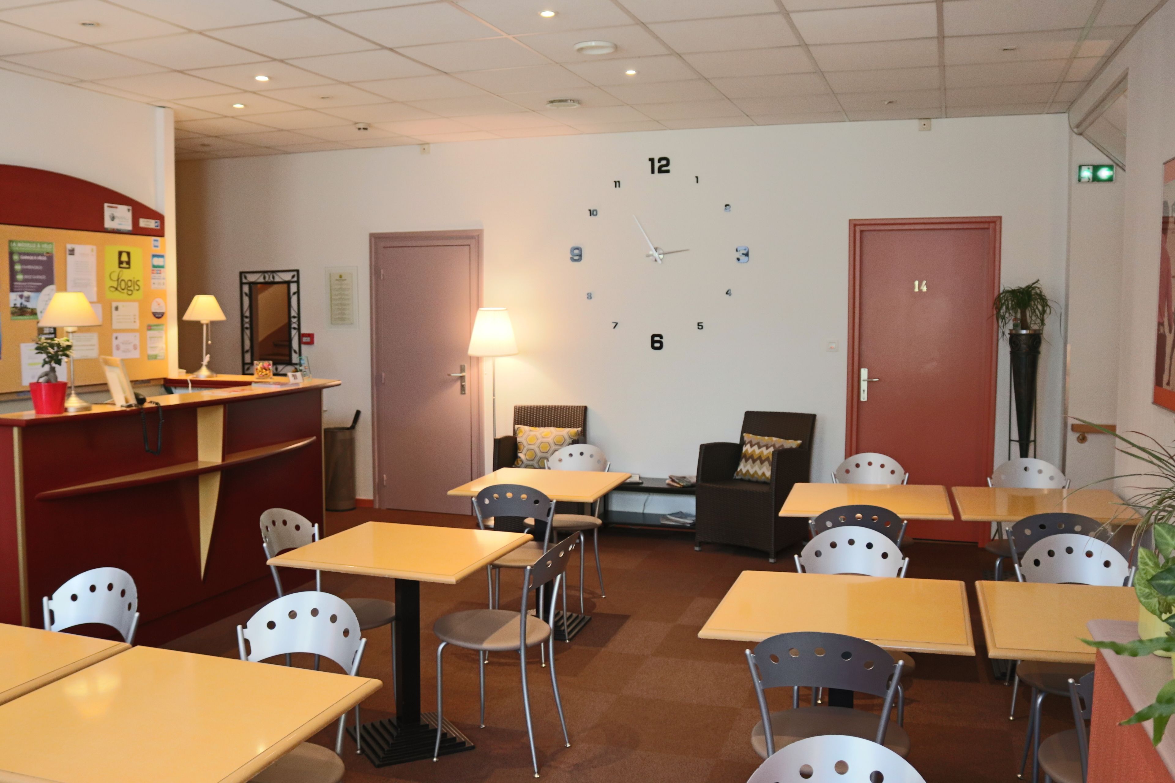 A hotel lobby with a reception desk, multiple tables and chairs, a clock on the wall, and a few potted plants.