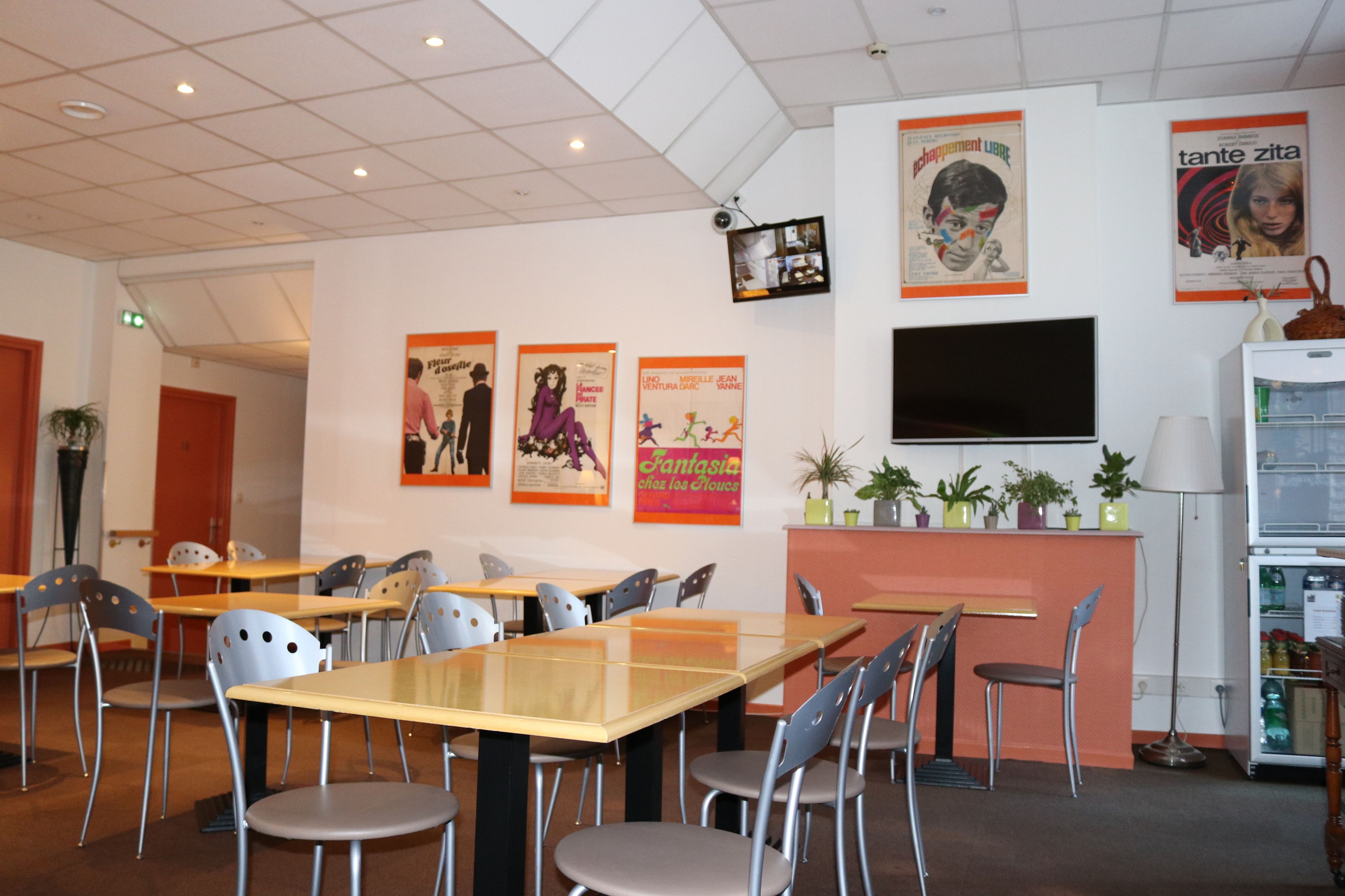 Ein Restaurant mit Tischen, Stühlen, Postern an der Wand, einem Fernseher und einem Kühlschrank.