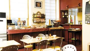 Zona de desayuno de hotel con mesas, sillas, estación de café y una exhibición de frutas.