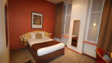 Una habitación de hotel con una cama grande, una mesita de noche con lámpara, una ventana con cortinas e imagen enmarcadas en la pared.