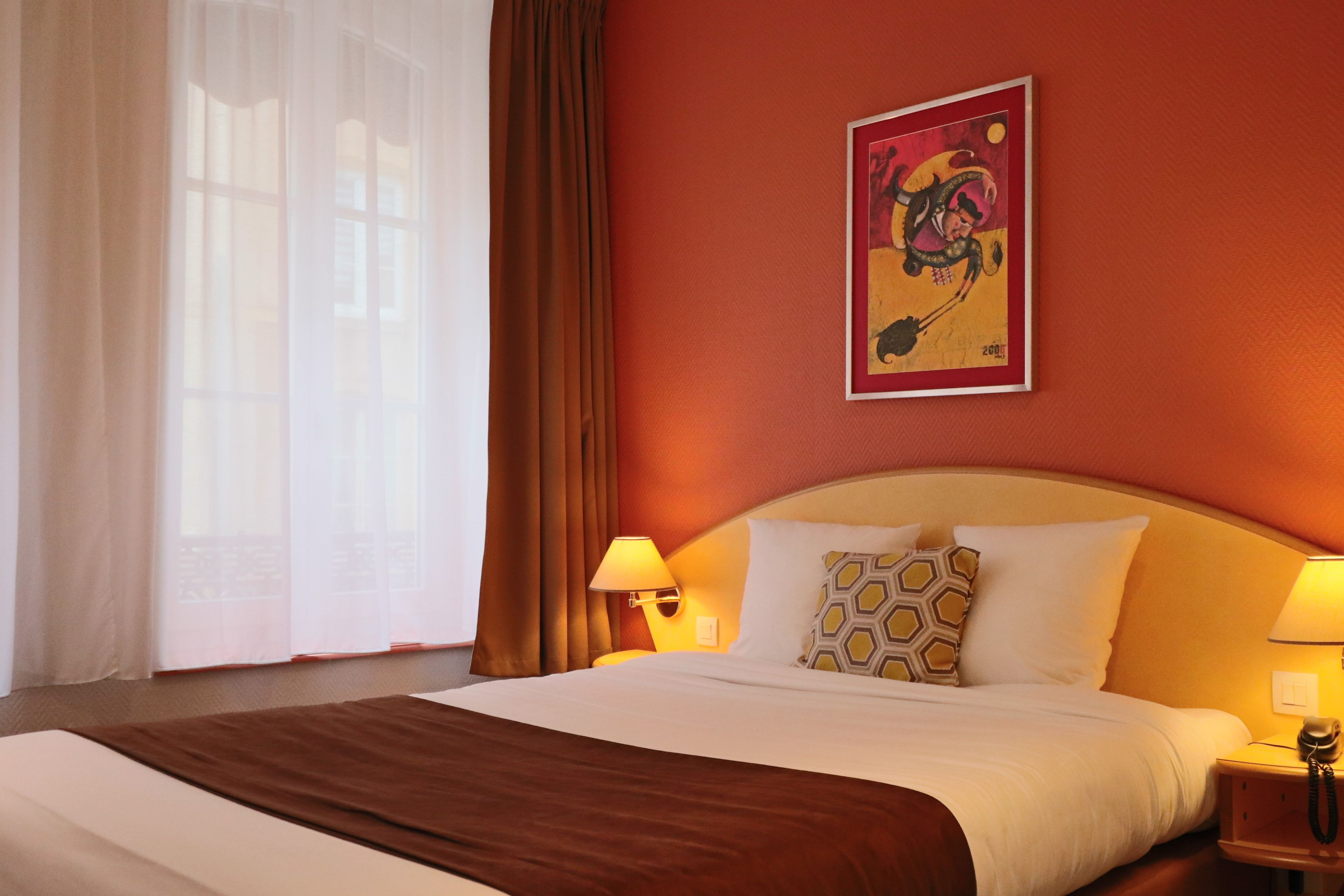 Habitación de hotel con una cama grande, dos lámparas de noche, una obra de arte colgada en la pared y una ventana con cortinas.