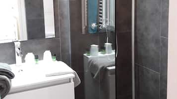 A modern bathroom with a glass-enclosed shower, a white sink with toiletries, and a mirror above the sink.