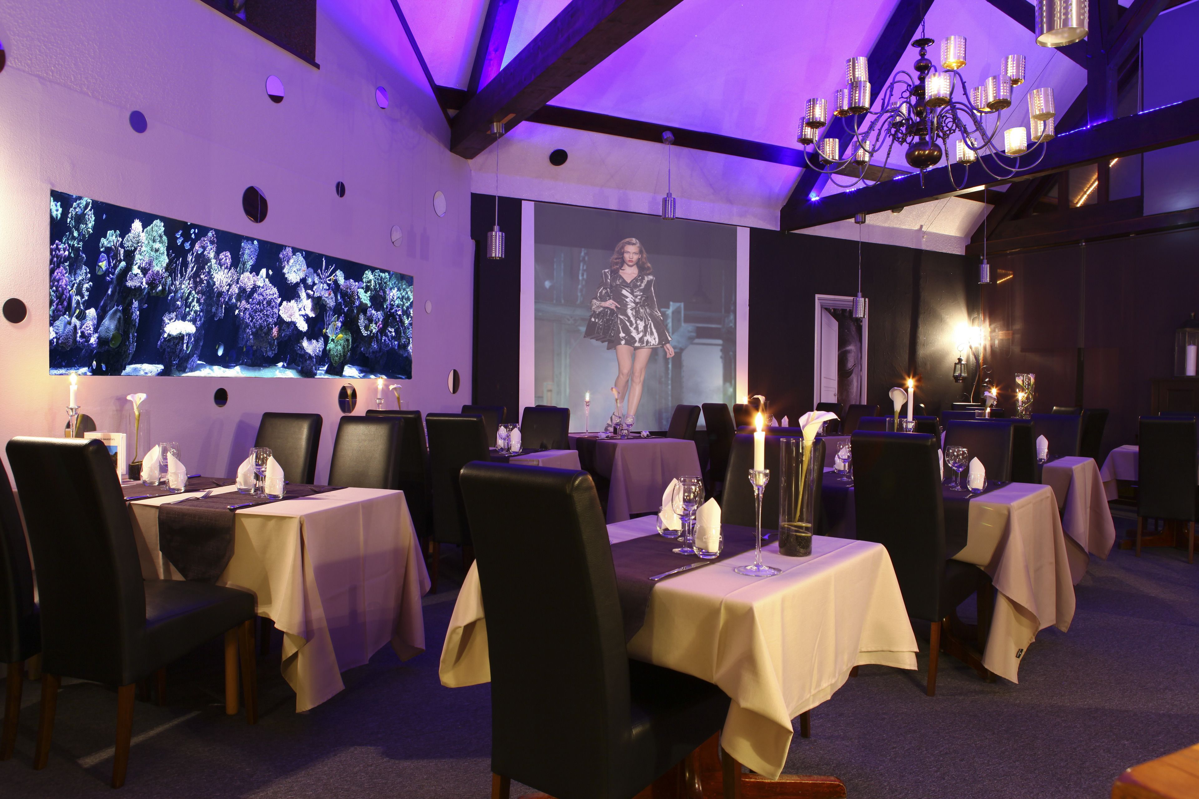 Un restaurant avec des tables dressées pour le service, un grand aquarium et un lustre.