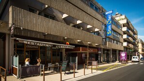 A hotel with a modern facade, a restaurant named 'L'ESCAPADE' on the ground floor, and a sign indicating a 'Stimotel' on the upper level.