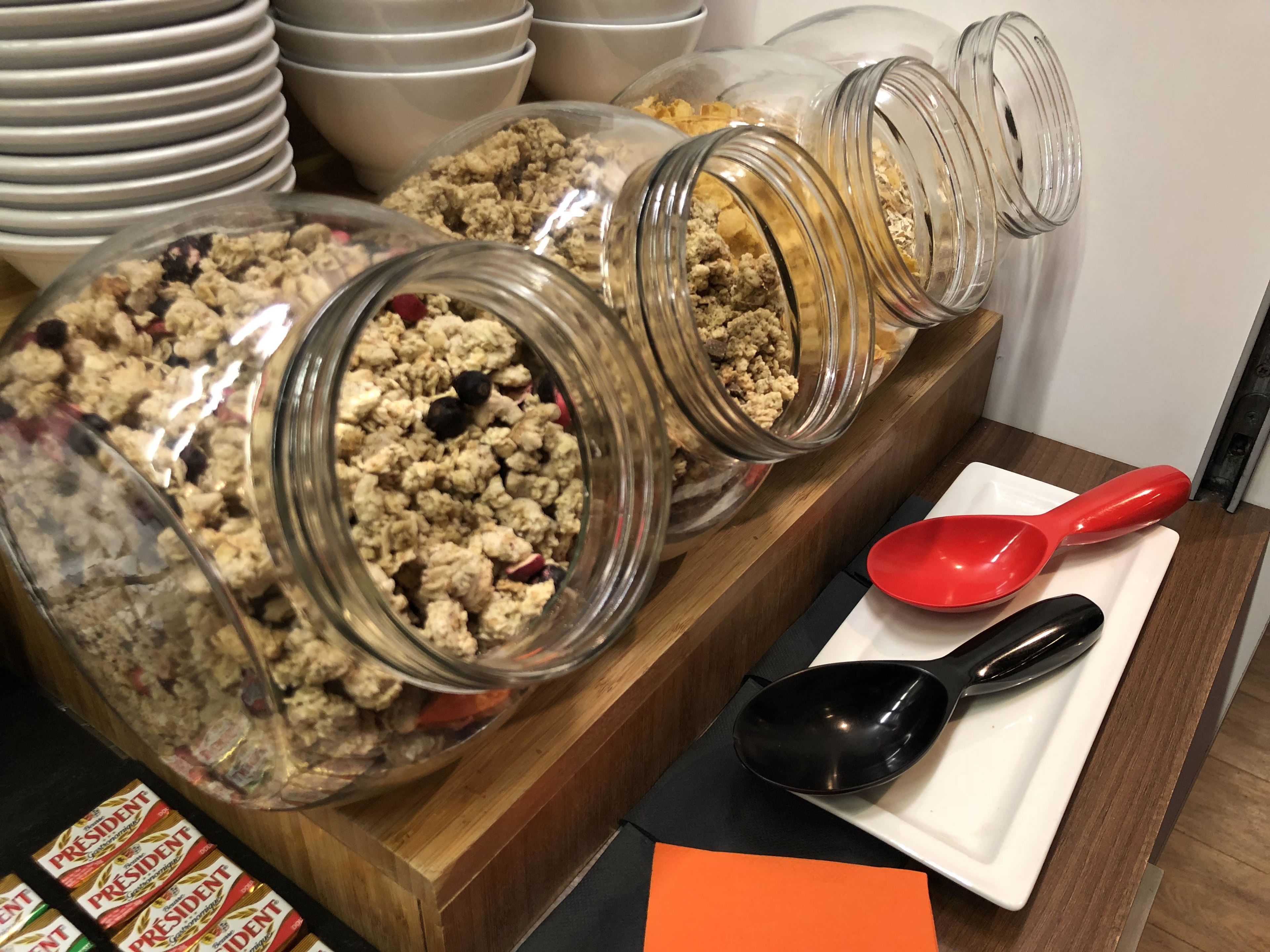 A buffet setup with various food items in glass jars and bowls, a red and black serving spoon, and President cereal boxes.