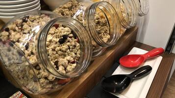 A buffet setup with various food items in glass jars and bowls, a red and black serving spoon, and President cereal boxes.