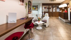 A reception area with a wooden reception desk, white chairs, a red stool, and a clock on the wall.
