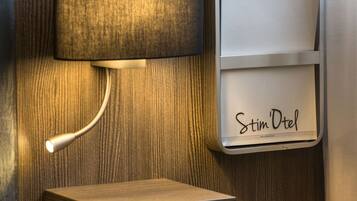 Uma luminária fixada na parede e um minibar com a inscrição 'Stim Dotel'.