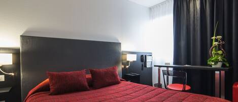 Habitación de hotel con una cama grande, un escritorio con silla, un teléfono y una mesita con una planta.