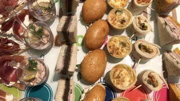 A variety of finger foods including sandwiches, rolls, and appetizers, arranged on a colorful tablecloth.