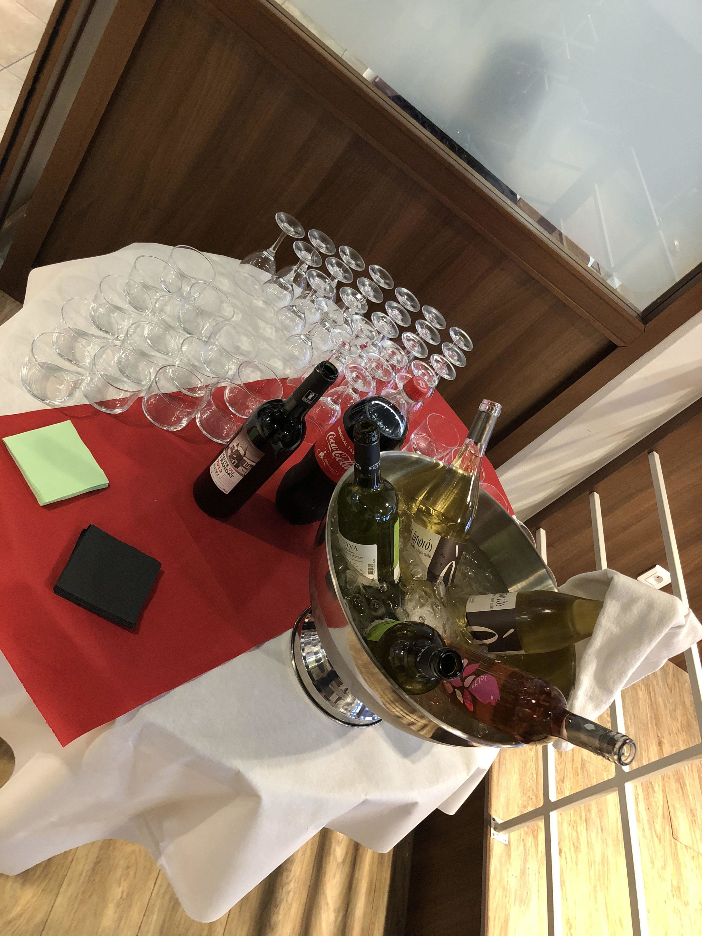 Una mesa con un mantel rojo, un camino de mesa blanco y una bandeja metálica con botellas de vino y copas.