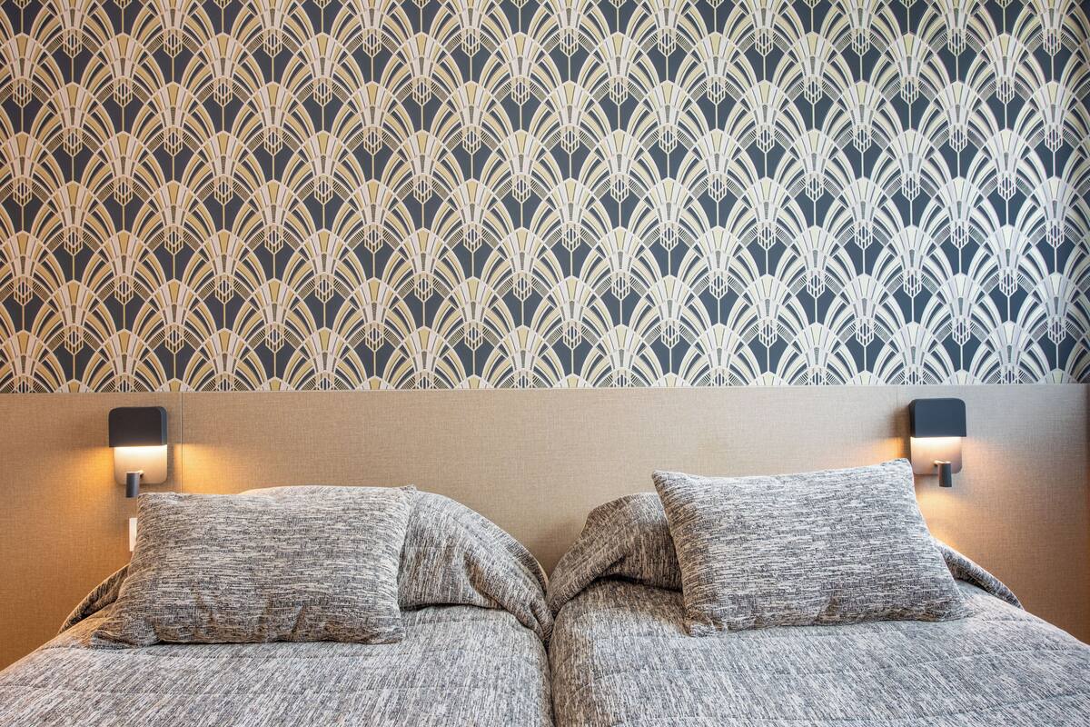 A bed with two pillows, a headboard, and a wall with a patterned wallpaper.