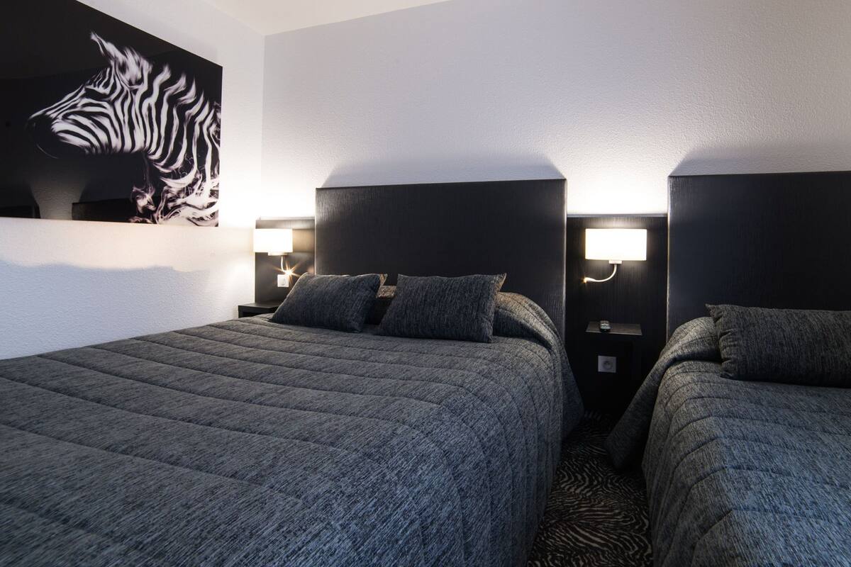 A hotel room with two beds, a zebra mural, and wall-mounted lights.