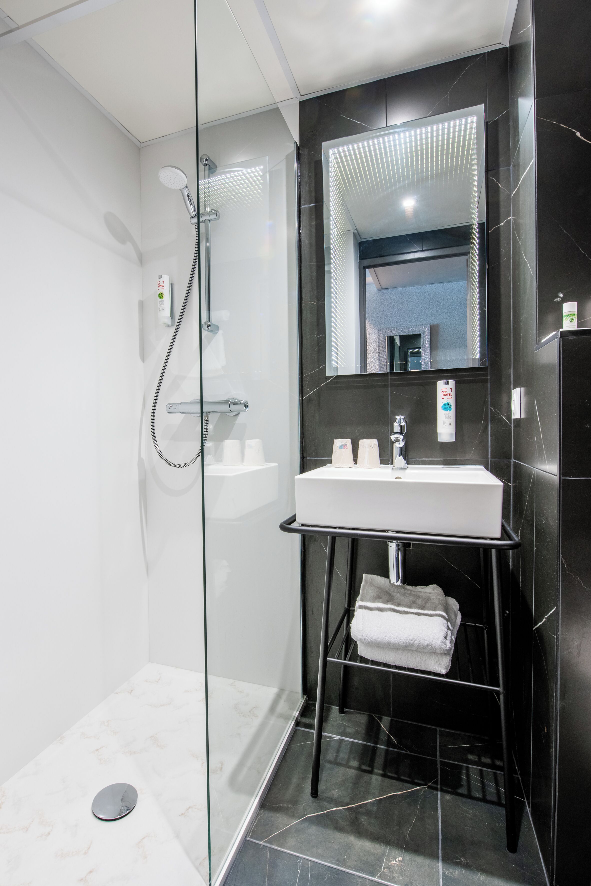 A modern bathroom with a glass-enclosed shower, a white sink, and a black marble wall.