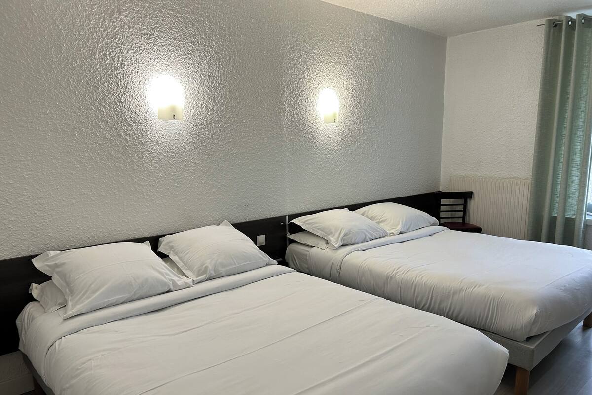 Two single beds with white linens in a room with textured white walls and two wall-mounted lights.
