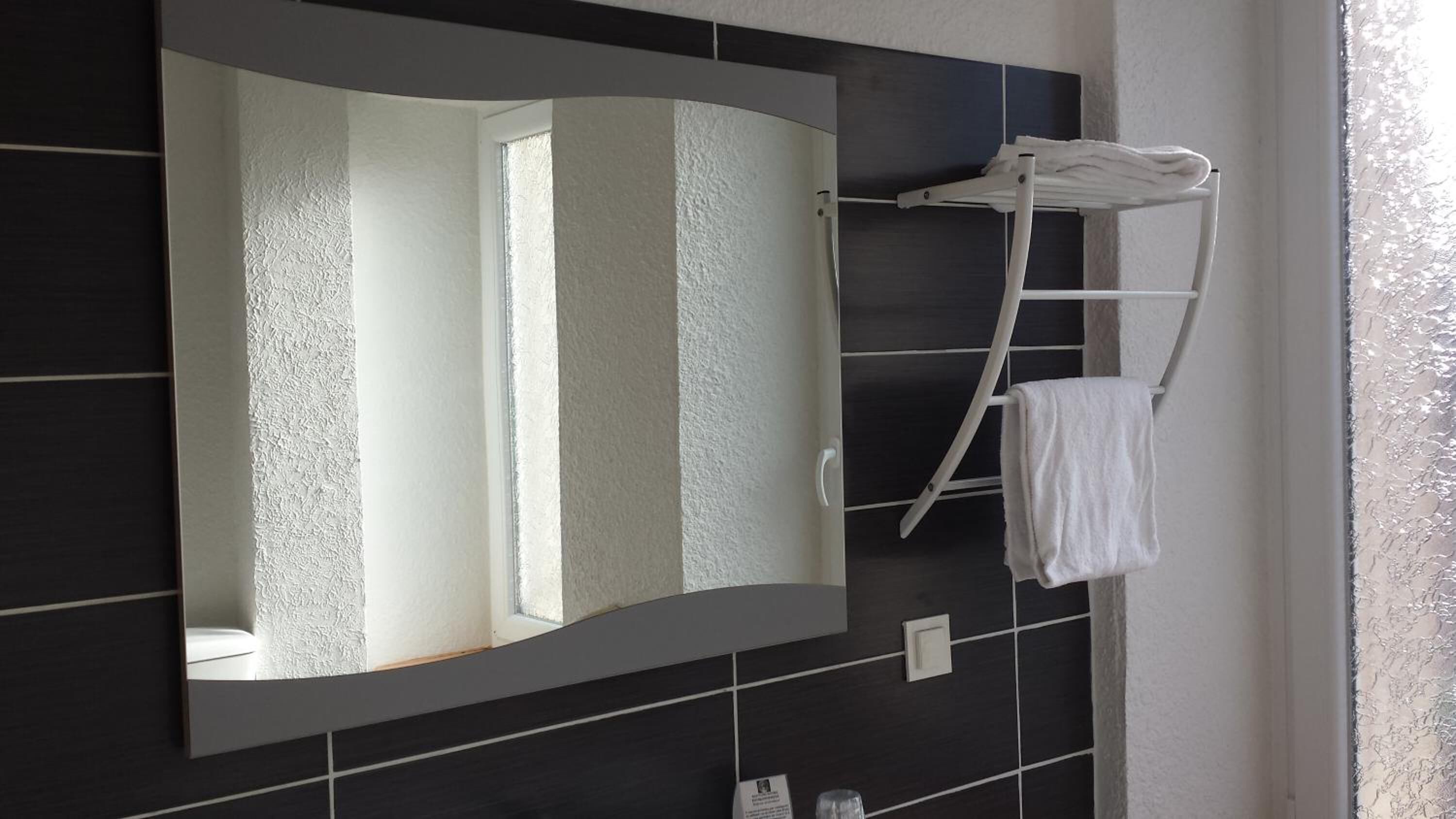 A bathroom with a large mirror, dark tiles, and a towel rack with a towel.