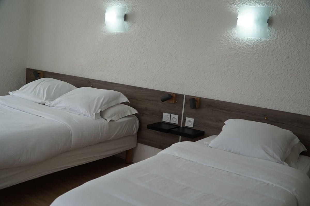 Two single beds with white linens, a wooden headboard, and two wall-mounted light fixtures.