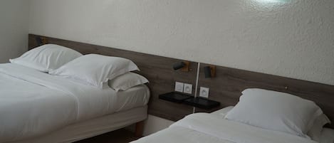 Two single beds with white linens, a wooden headboard, and two wall-mounted light fixtures.