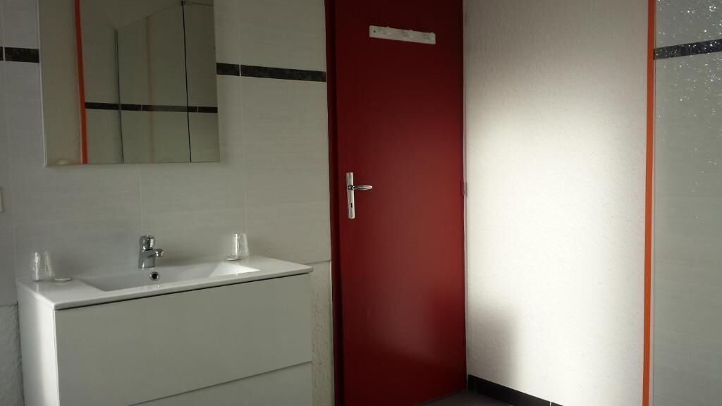 Une salle de bain avec un lavabo blanc, un miroir et une porte rouge.