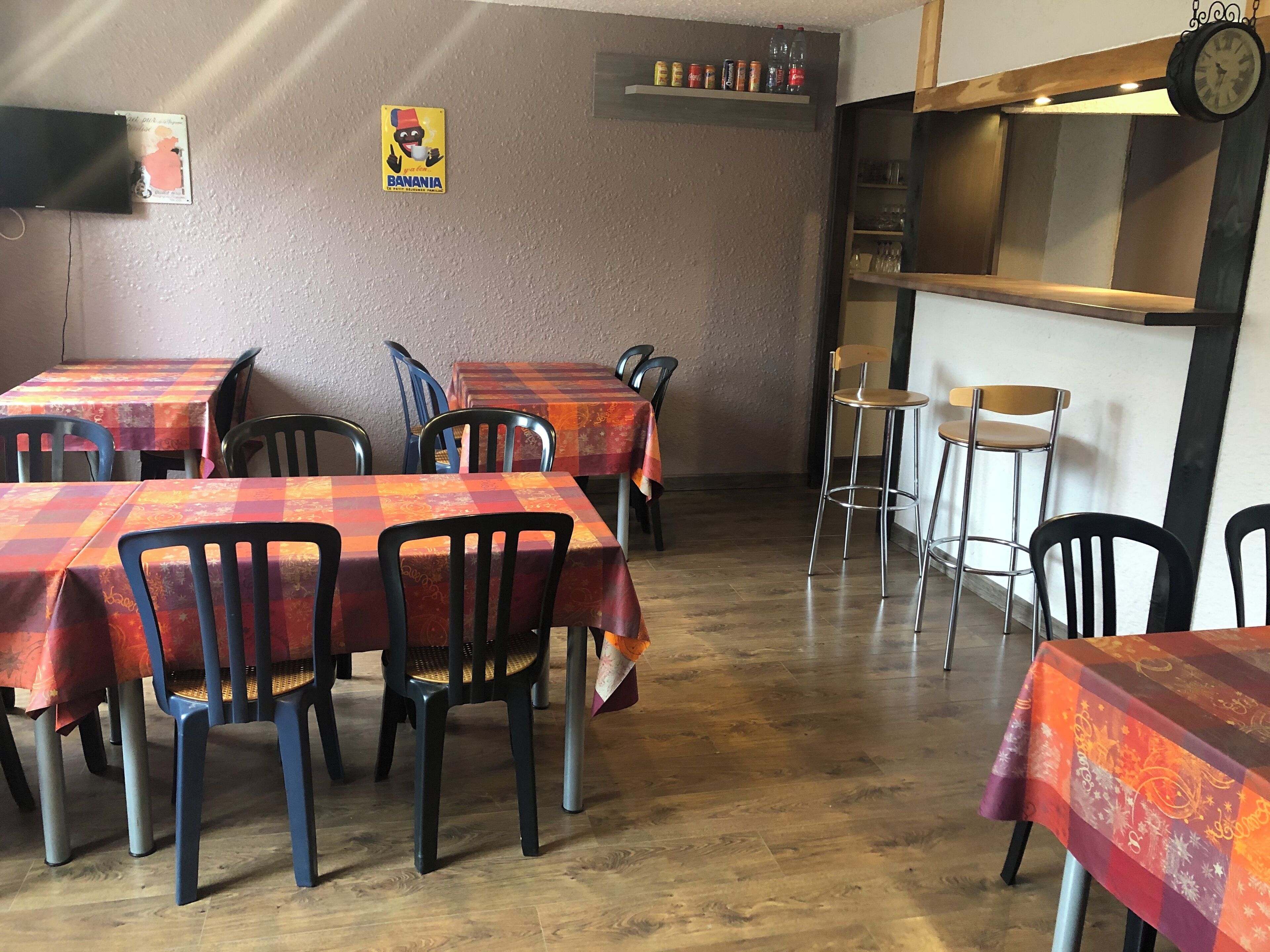 L’intérieur d’un restaurant présente de nombreuses tables recouvertes de nappes à carreaux rouges et oranges, des chaises noires et un plancher en bois.