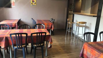 A restaurant interior with multiple tables covered in red and orange checkered tablecloths, black chairs, and a wooden floor.