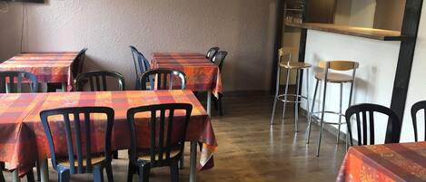 Interior de un restaurante con varias mesas cubiertas con manteles a cuadros rojos y naranjas, sillas negras y piso de madera.
