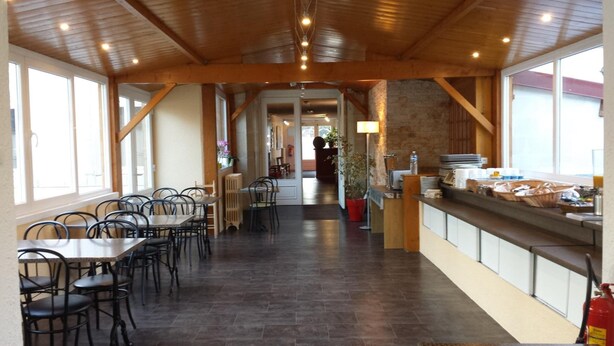 A restaurant with a long counter, multiple tables, and chairs. There is a kitchen area visible in the background. - Citotel Du Tigre (Verdun)